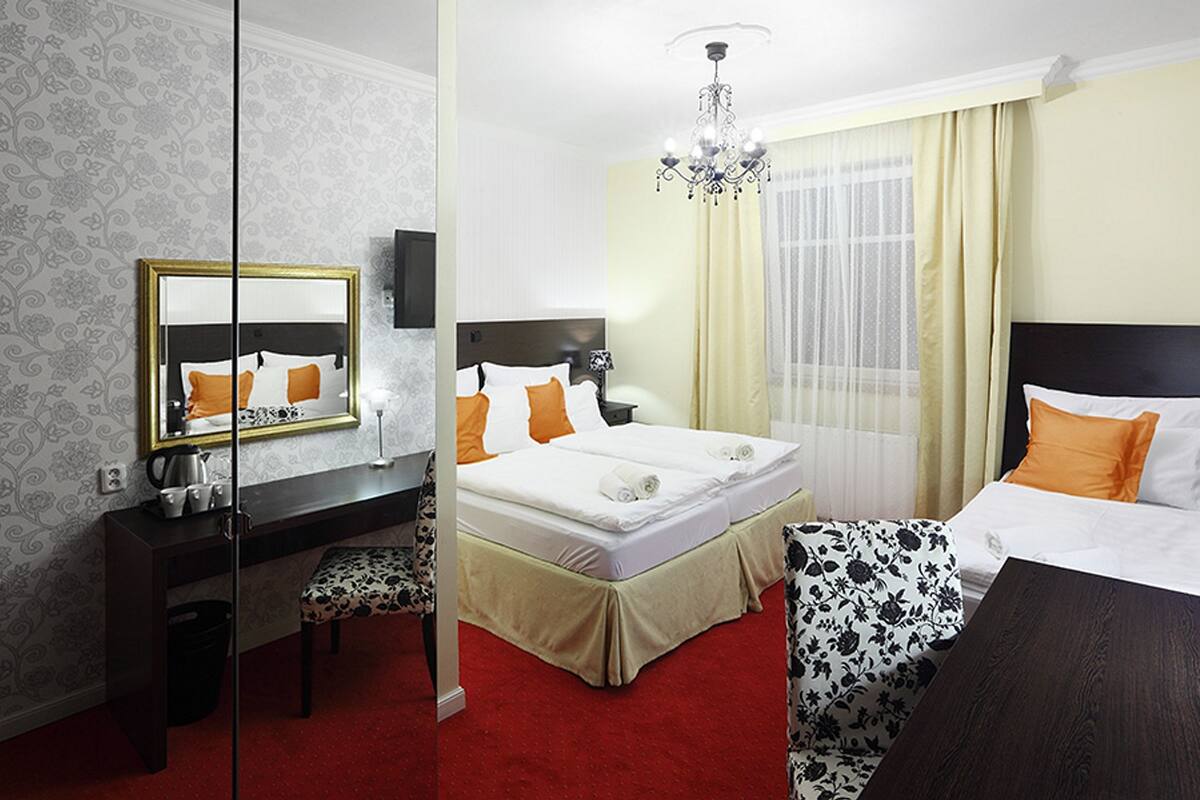 A hotel room with a large bed, a desk with a mirror, a chandelier, and a red carpet.