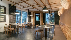 Un interior de restaurante moderno con mesas y sillas de madera, iluminación colgante y vistas al exterior a través de amplios ventanales.