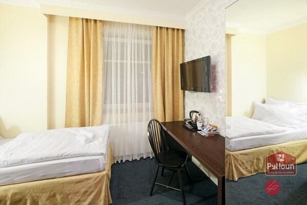 A hotel room with two beds, a desk, a chair, a TV, and a window with curtains.