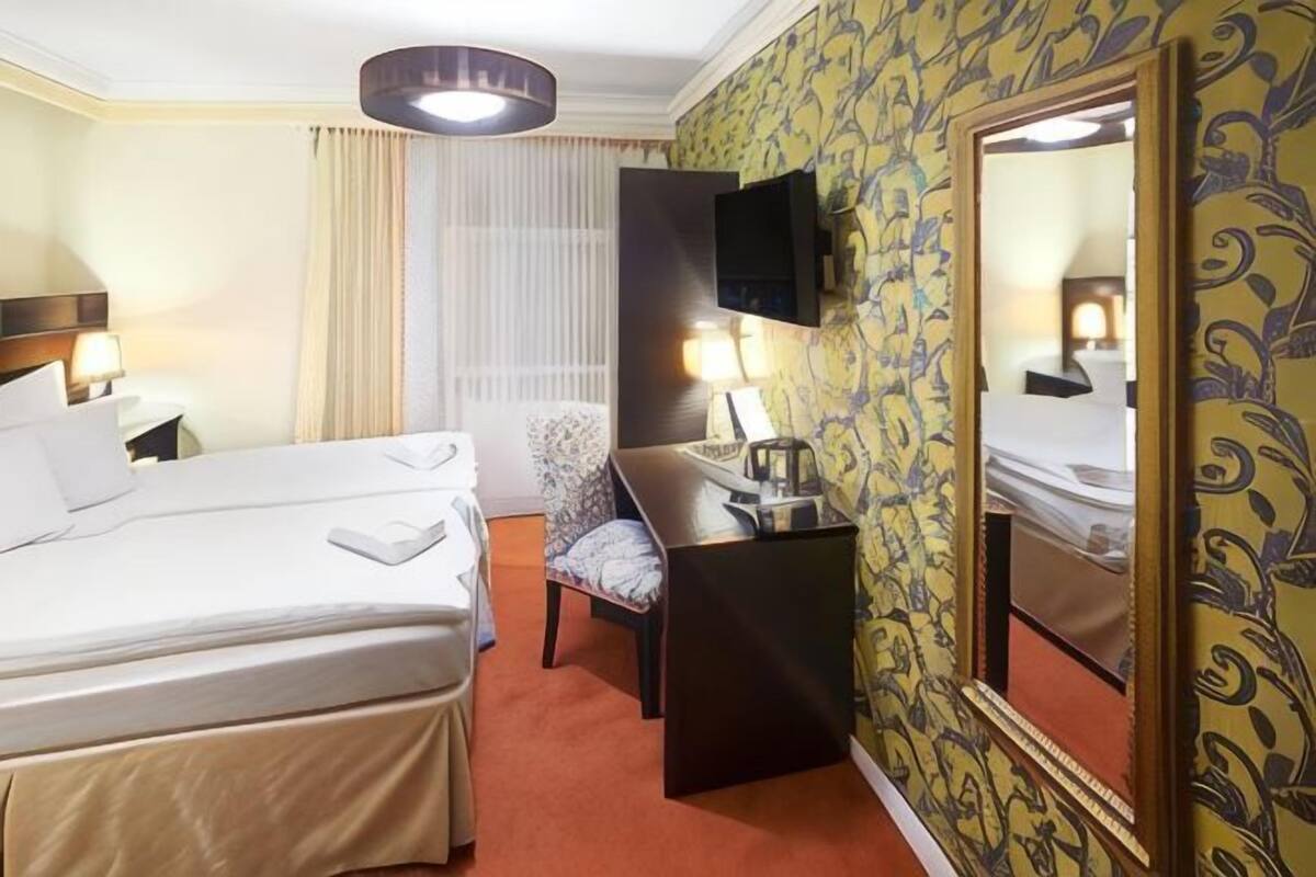 A hotel room with two beds, a desk, a chair, a TV, and a large mirror.