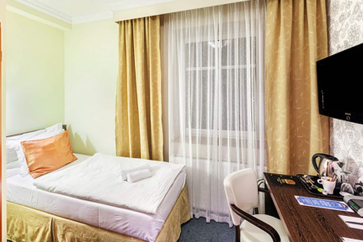 A hotel room with a bed, a desk, a chair, a television, and a window with curtains.