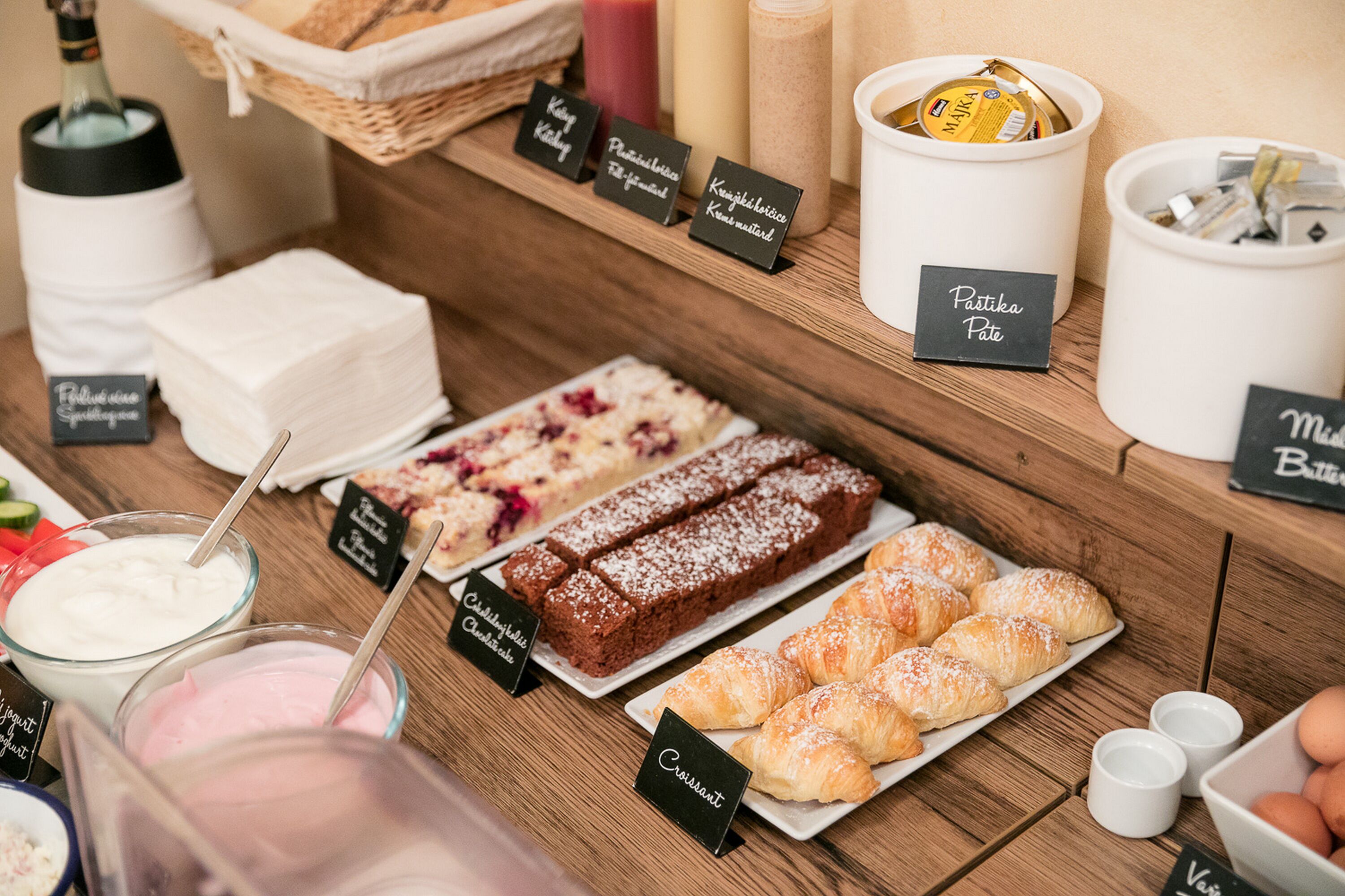 A variety of desserts and beverages on a wooden table, including cakes, pastries, and a bottle of wine.
