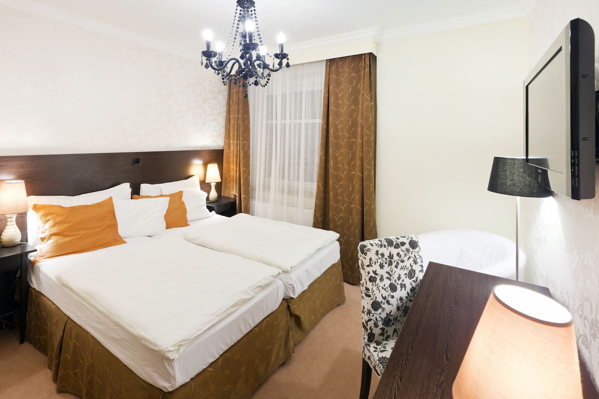 A hotel room with two beds, a chandelier, a desk with a lamp, and a chair.
