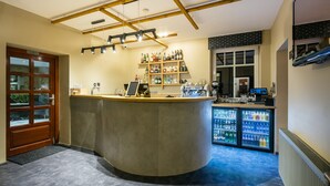 Zona de bar con mostrador de madera, estanterías con botellas y un refrigerador con bebidas.