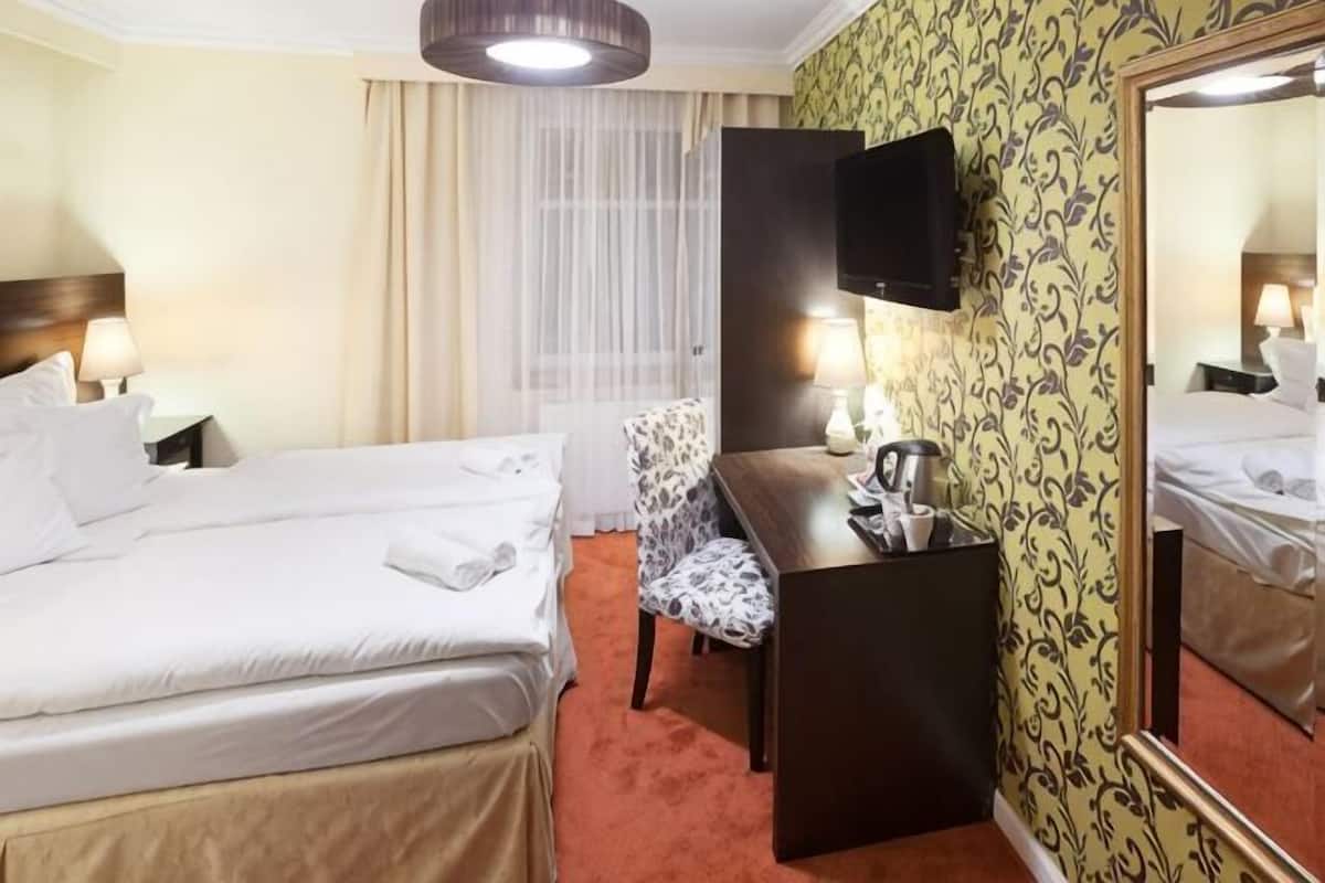 A hotel room with two beds, a desk, a chair, a television, and a mirror.