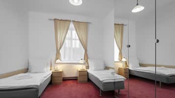 Een kamer met drie eenpersoonsbedden, een raam met gordijnen, nachtlampjes en een radiator.