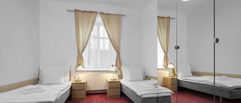 Una habitación con tres camas individuales, una ventana con cortinas, lámparas de noche y un radiador.