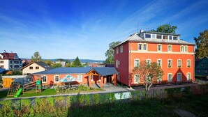 A red building with a blue roof, surrounded by greenery and other houses.