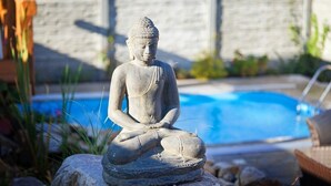 A stone Buddha statue in a garden setting with a pool in the background.