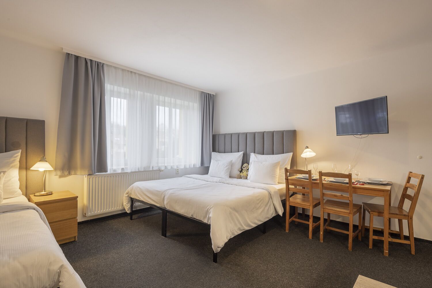 Hotellihuone, jossa on sänky, työpöytä tuoleineen, televisio ja ikkuna, jossa on verhot.
