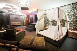 A spa room with a bed, wicker furniture, and a stone wall.