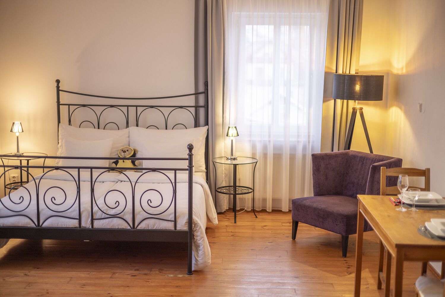 Een slaapkamer met een metalen bedframe, een stoel, een tafeltje en een lamp.