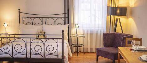Een slaapkamer met een metalen bedframe, een stoel, een tafeltje en een lamp.
