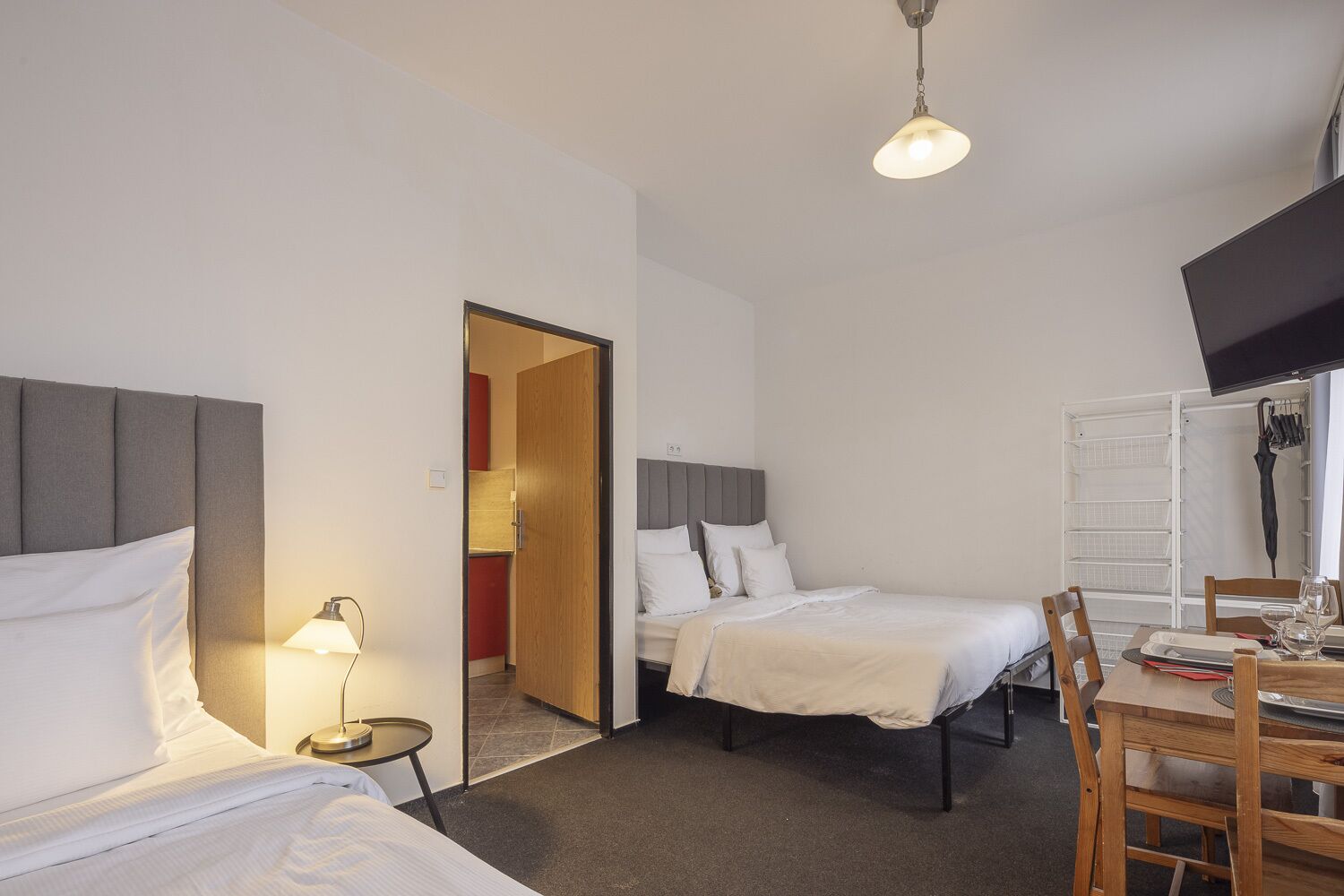 A hotel room with two beds, a desk with a chair, a TV, and a door leading to a bathroom.