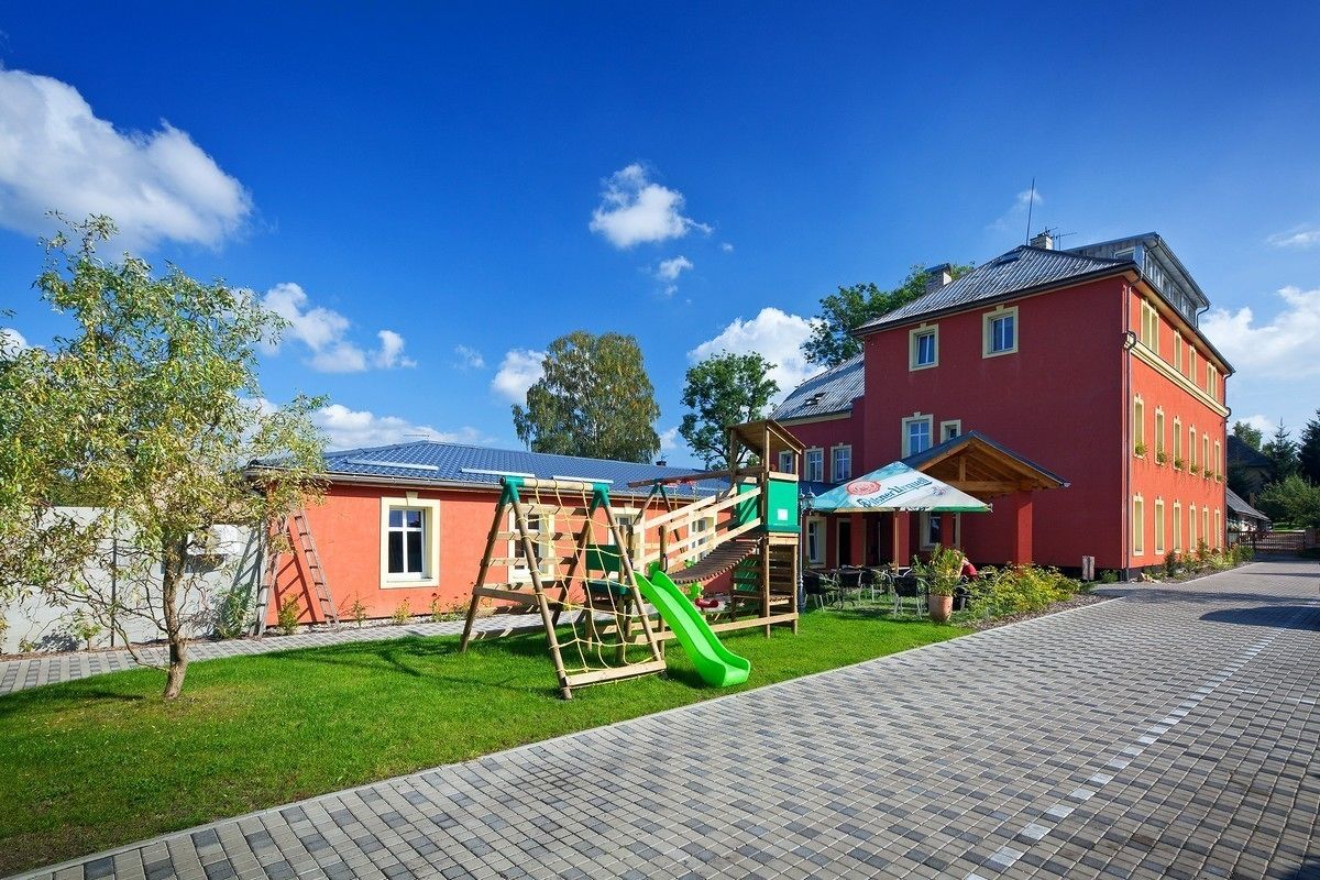 Un bâtiment rouge doté d’une aire de jeux, comprenant un toboggan et des balançoires, ainsi qu’un chemin pavé.
