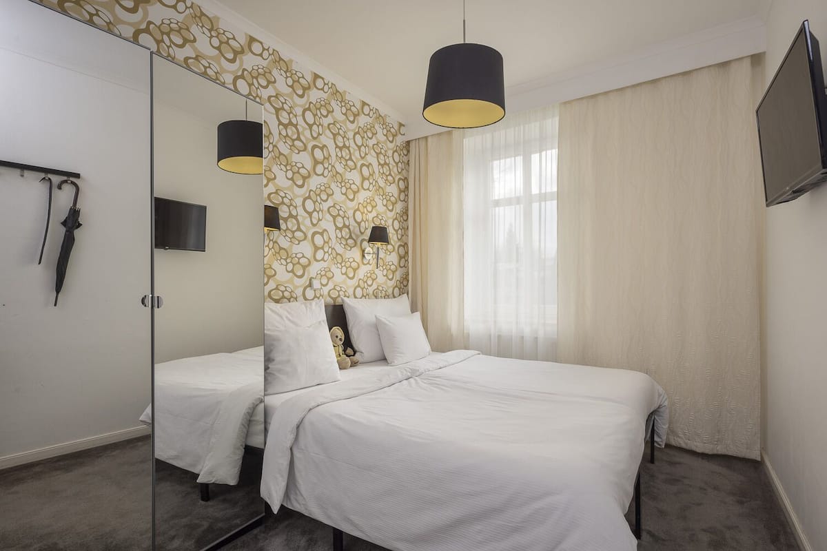 Habitación de hotel con cama, espejo, televisión y papel tapiz estampado.