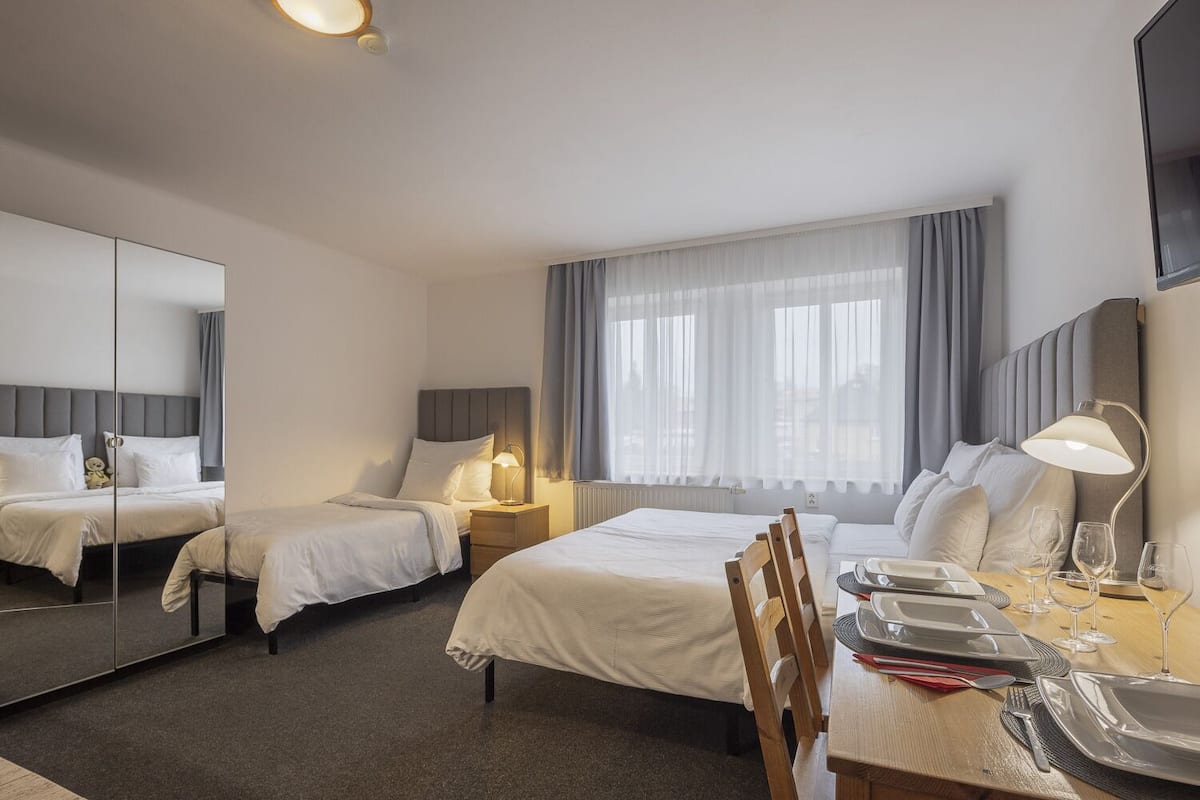 Habitación de hotel con dos camas, una mesa de comedor para dos personas, un espejo y una ventana con cortinas.