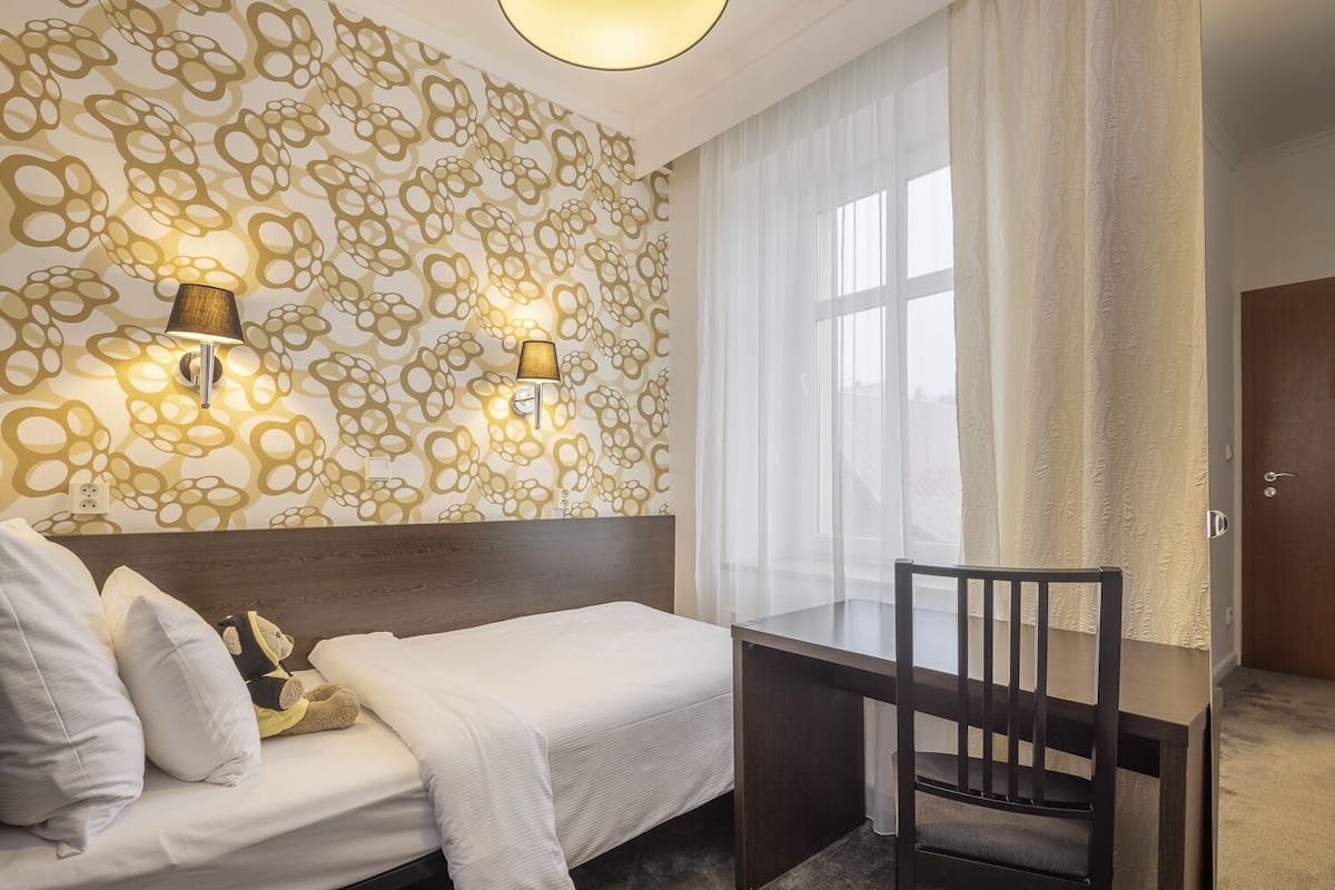 Habitación de hotel con una cama, un escritorio y dos lámparas fijadas a la pared.