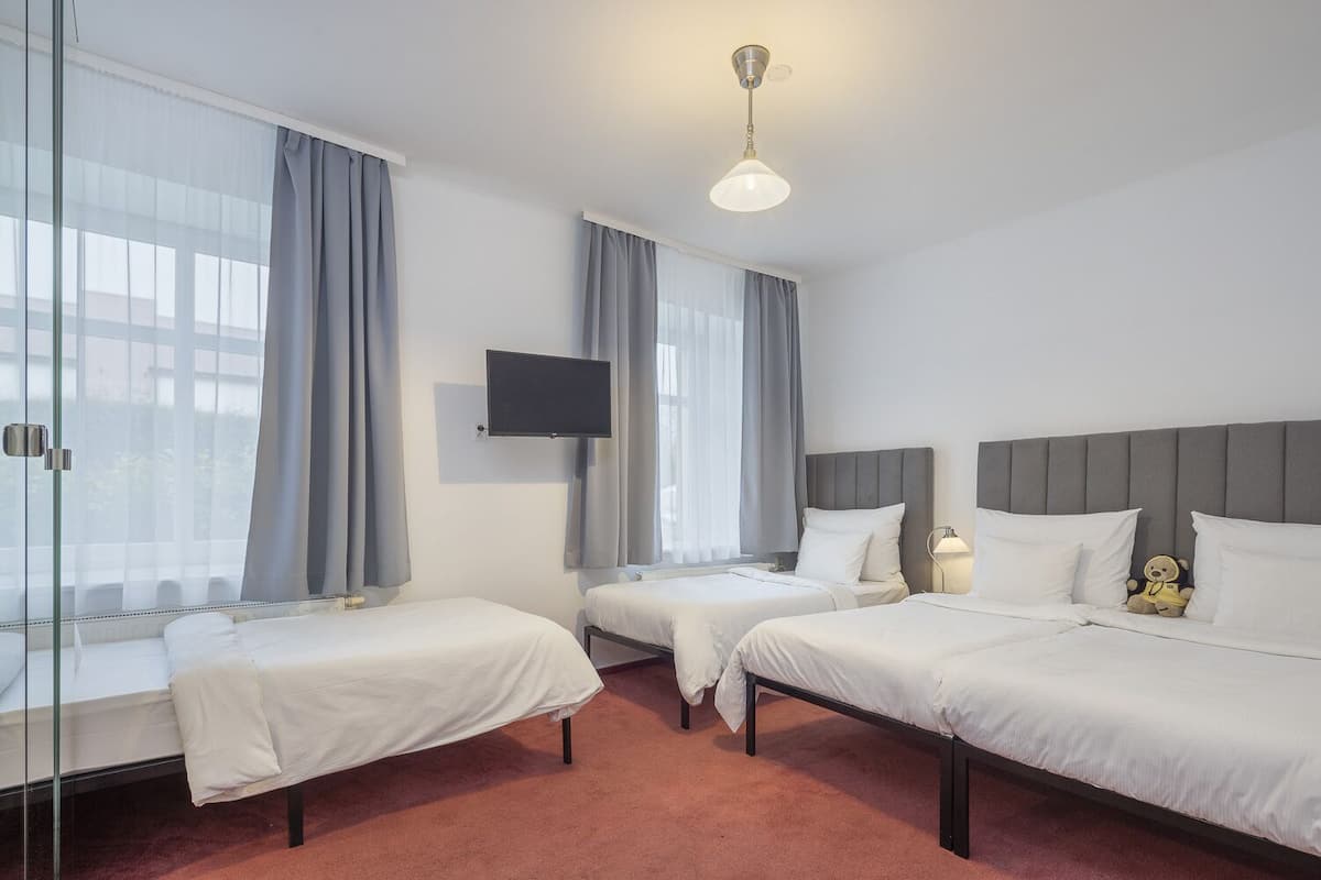 Habitación de hotel con dos camas individuales, un televisor montado en la pared y un ventilador de techo.