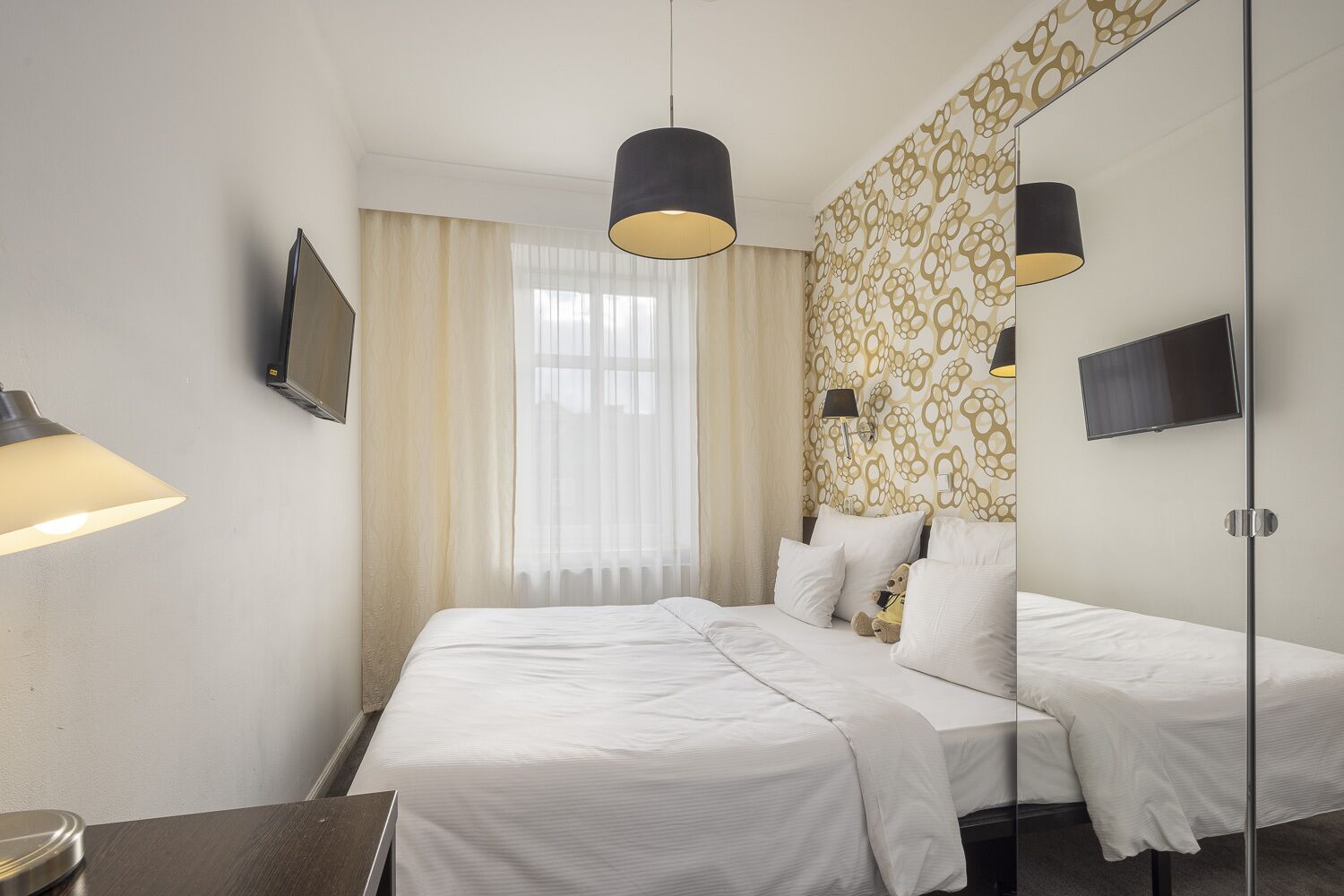 A hotel room with a large bed, two bedside tables, a TV, and a mirror.
