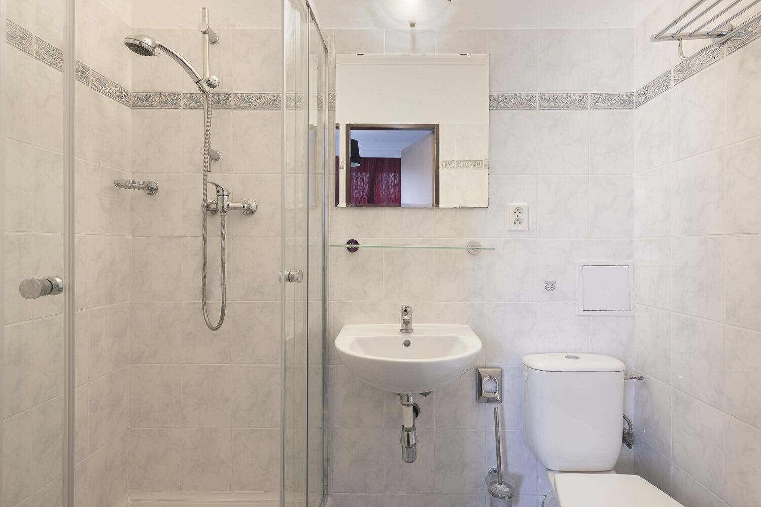 Een moderne badkamer met een douchecabine van glas, een witte wastafel en een toilet.
