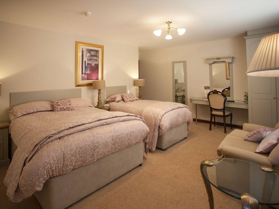 A hotel room with two beds, a desk, a chair, a mirror, and a glass table.