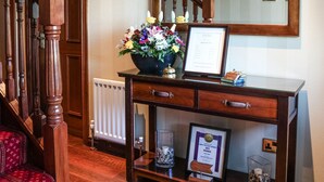 Een houten console tafel met een ingelijst certificaat, een bloemenvaas en een klein glazen potje met een kaars.