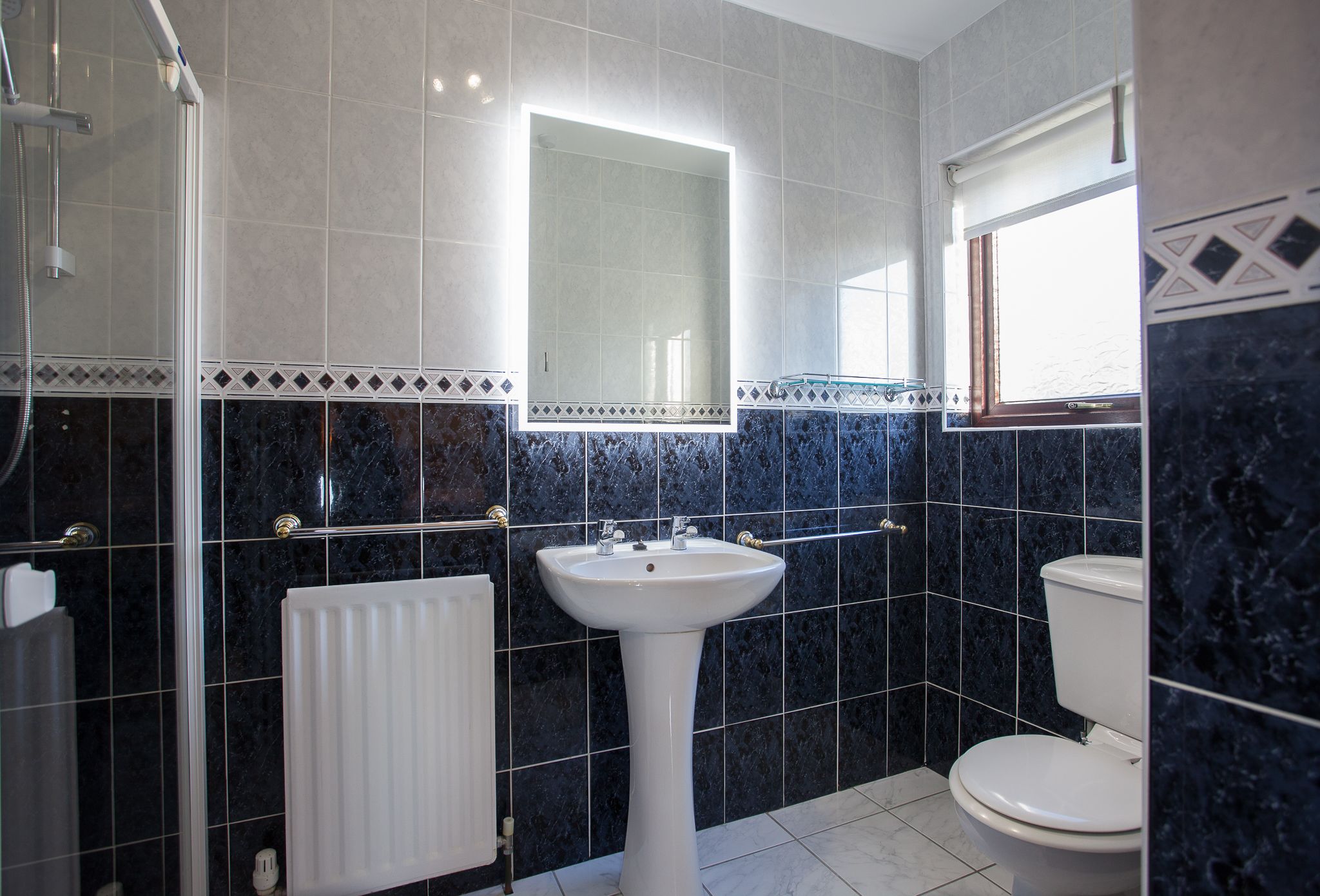 A bathroom with a white pedestal sink, a toilet, and a shower enclosure.