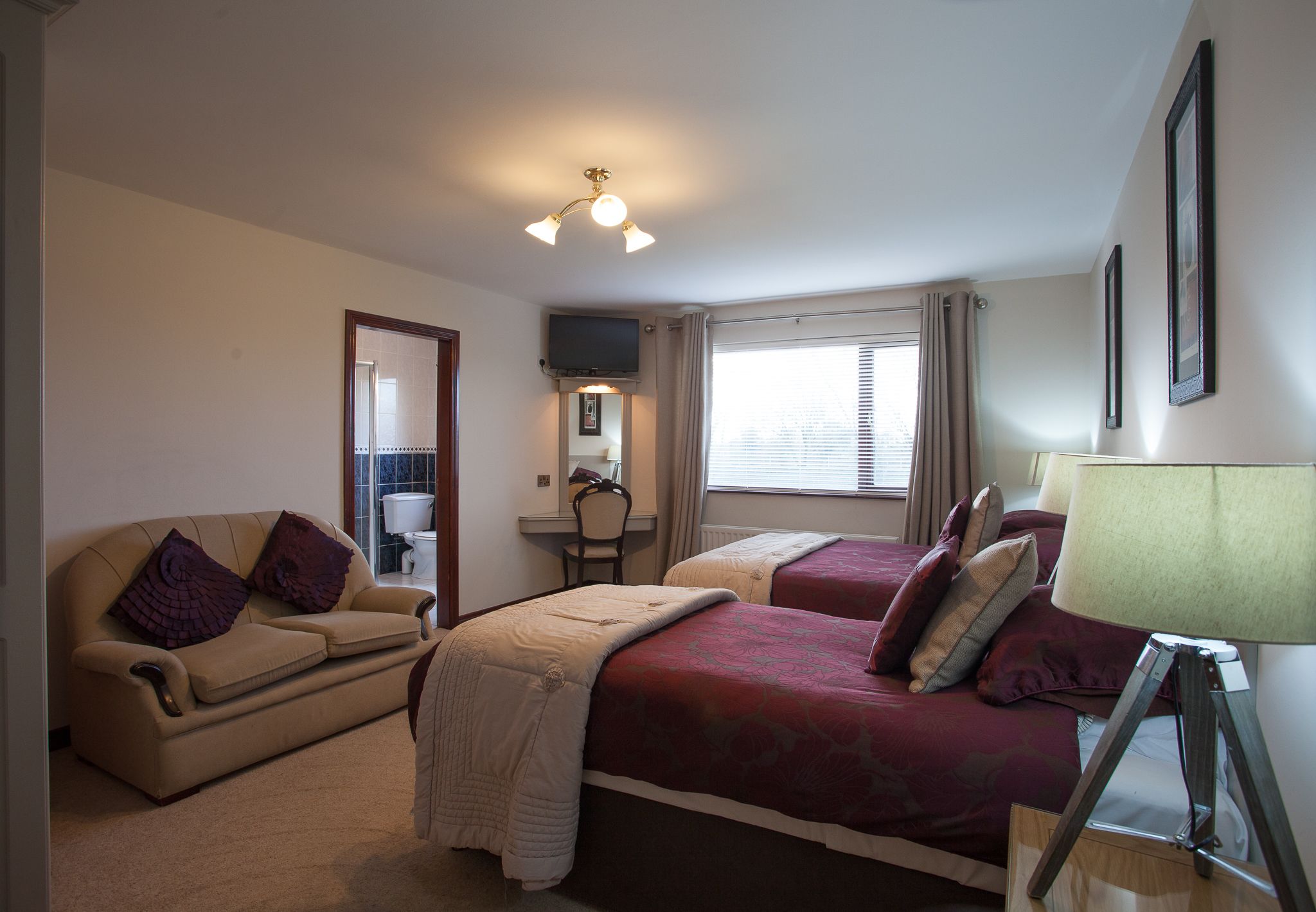 Une chambre d’hôtel avec deux lits, un canapé, un bureau, une chaise, une télévision et une fenêtre avec des rideaux.