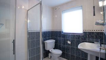Un baño con cabina de ducha de vidrio, inodoro y lavamanos.
