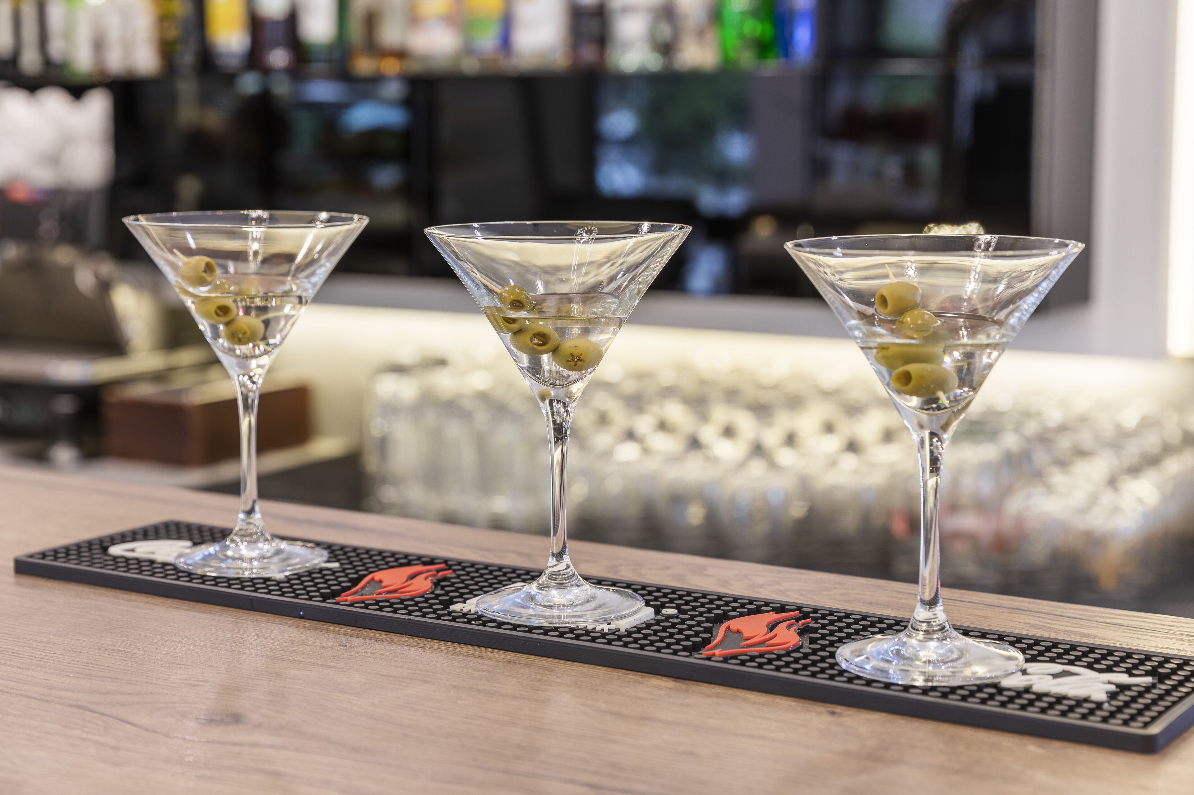 Three martini glasses with olives on a bar mat.