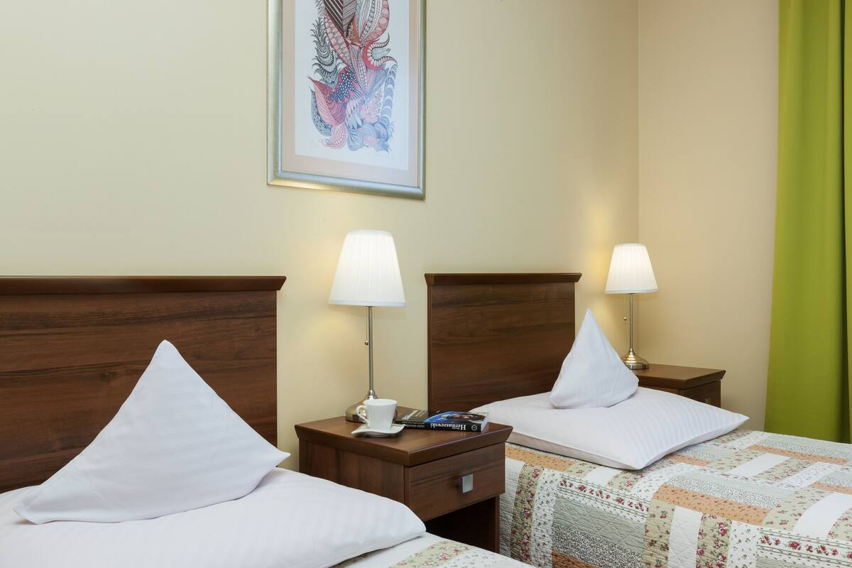 A hotel room with two beds, each with a white pillow and a nightstand with a lamp and a cup.