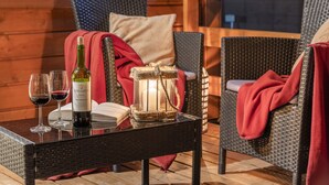 Uma cadeira de vime com um cobertor vermelho, uma garrafa de vinho e duas taças de vinho sobre uma mesa.
