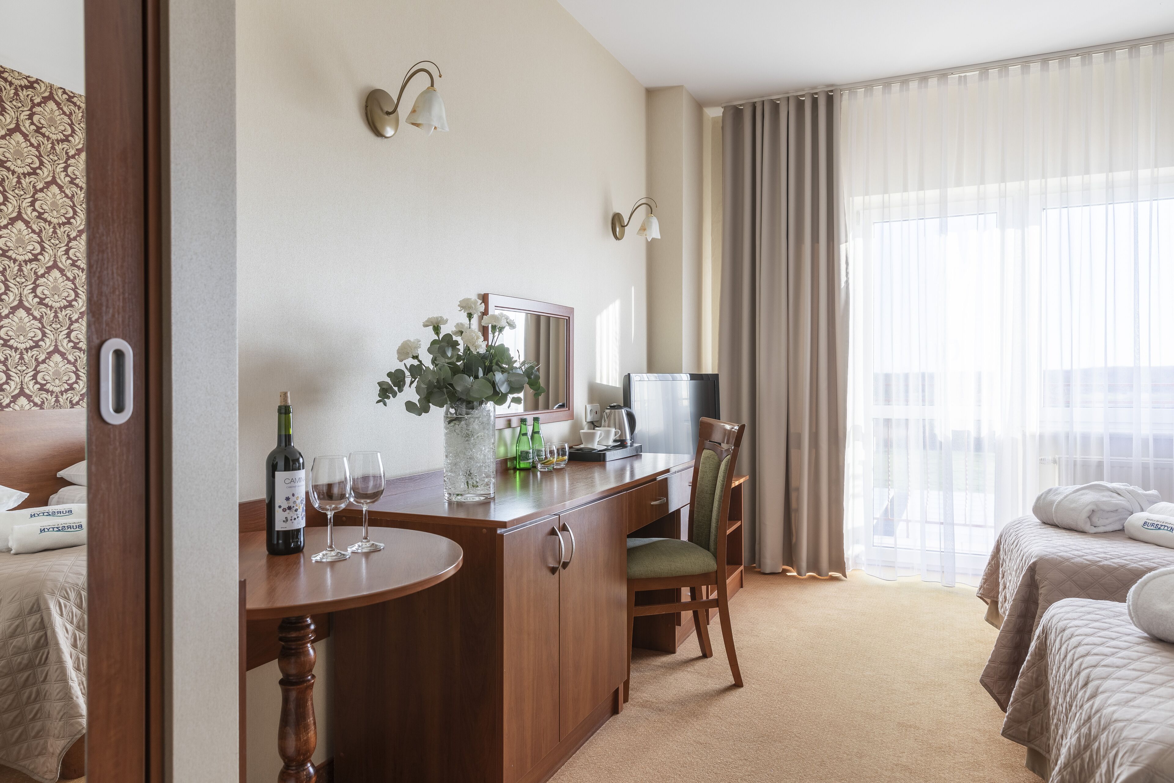 Une chambre d’hôtel comprenant un lit, un bureau avec une chaise, un miroir, une fenêtre avec des rideaux et un minibar.