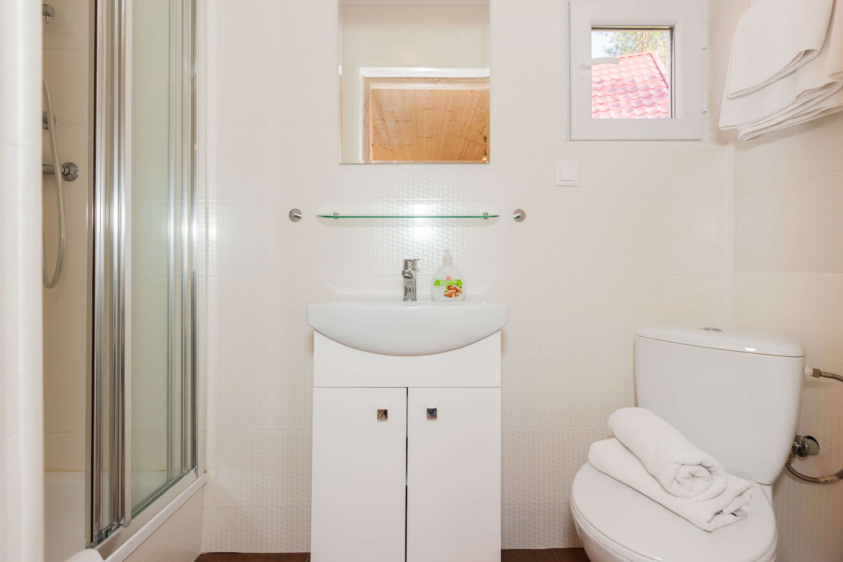 Un bagno con cabina doccia in vetro, lavandino bianco con dispenser di sapone e water con un asciugamano sopra.