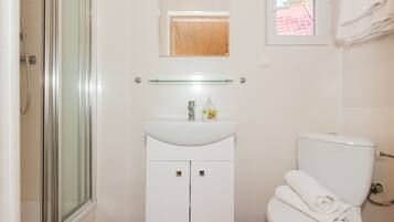 Un bagno con cabina doccia in vetro, lavandino bianco con dispenser di sapone e water con un asciugamano sopra.