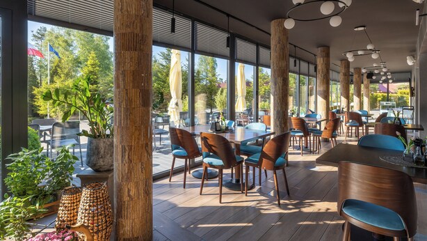 Um restaurante moderno com pilares de madeira, janelas amplas e diversos tipos de assentos.
