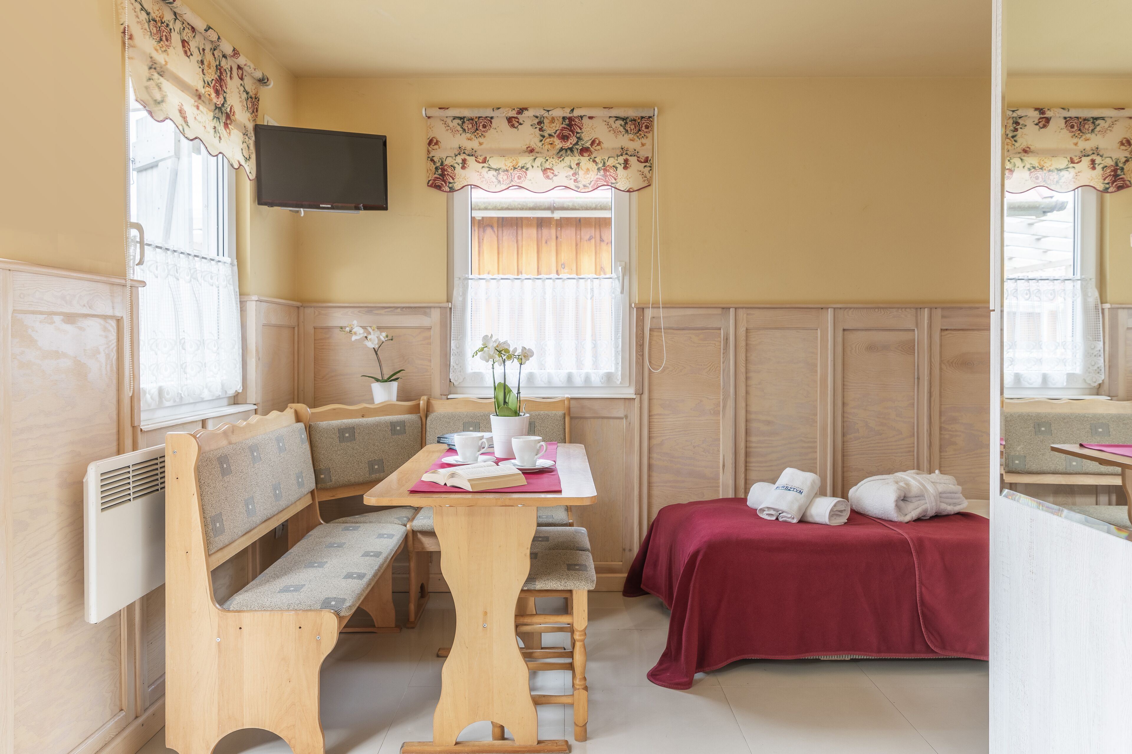 Una habitación acogedora con una zona de estar con banco de madera, una mesita con una planta y una cama con manta roja.