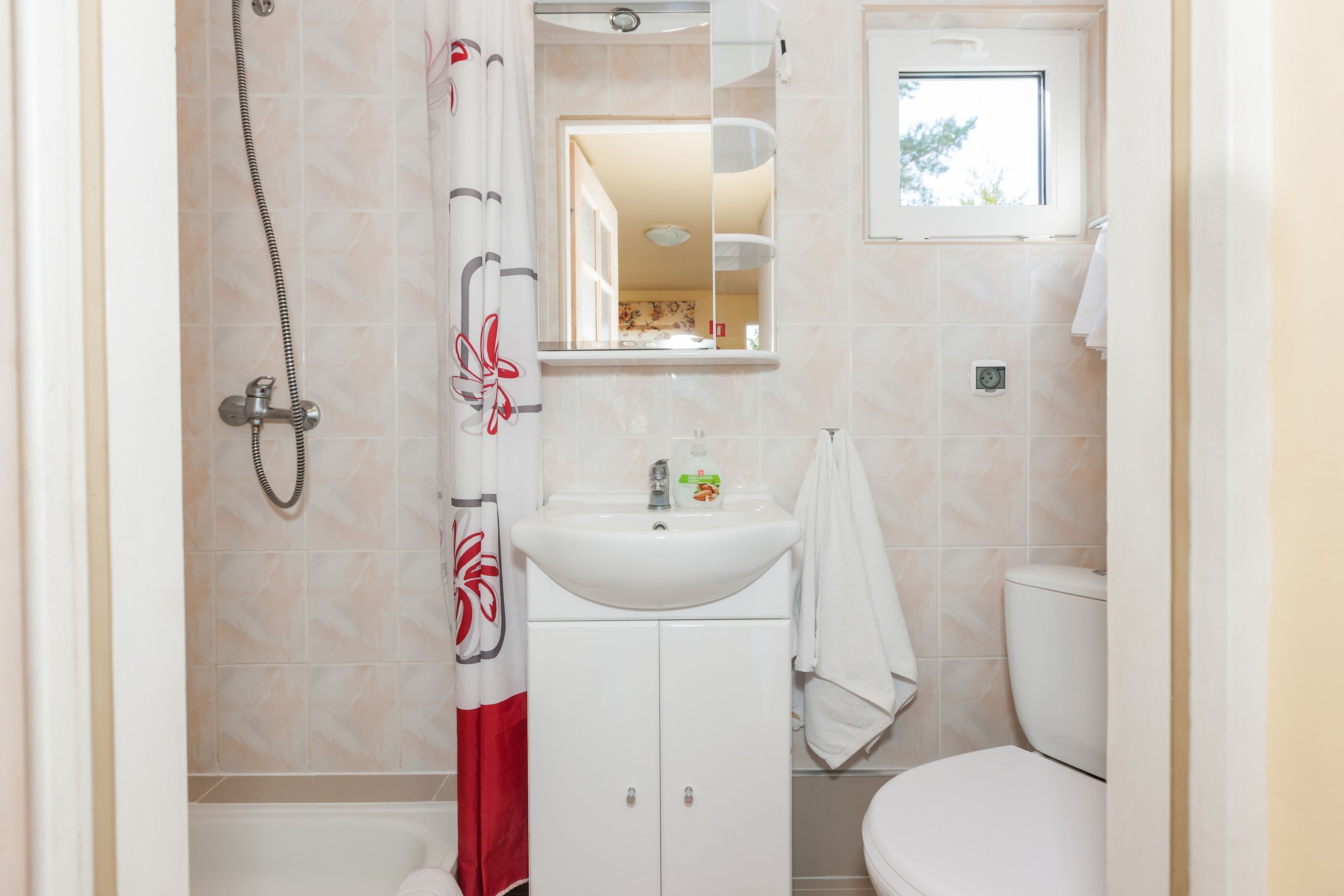 A bathroom with a shower, sink, toilet, and a window.