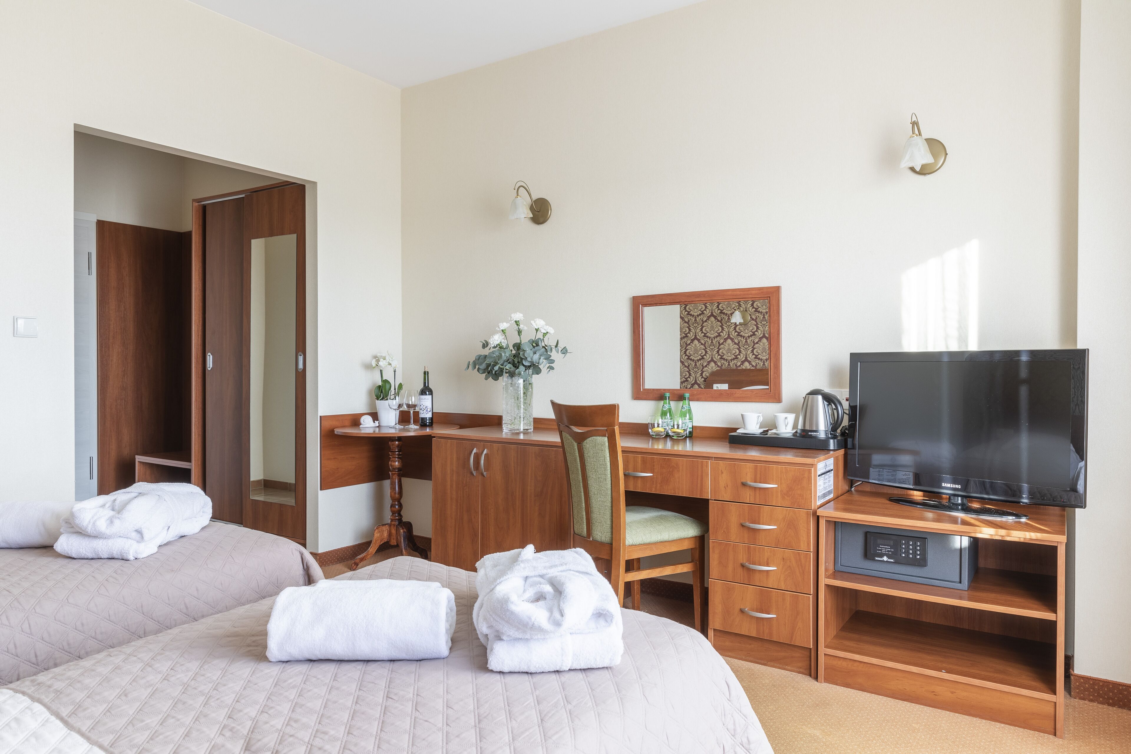 Camera d'albergo con due letti, una scrivania con televisione, una sedia, uno specchio e un punto luce a parete.
