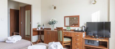 Habitación de hotel con dos camas, un escritorio con televisor, una silla, un espejo y una lámpara fijada a la pared.