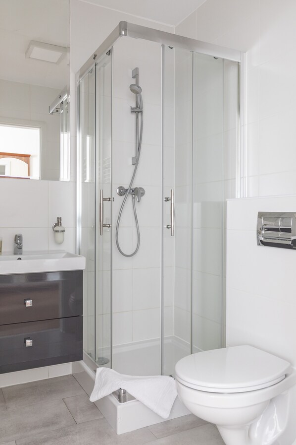 Un baño moderno con ducha de vidrio, inodoro blanco y tocador oscuro.