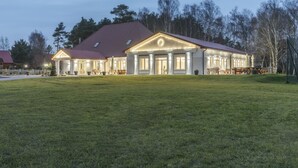 Um edifício amplo e bem iluminado, com fachada simétrica, telhado vermelho e um gramado espaçoso na frente.
