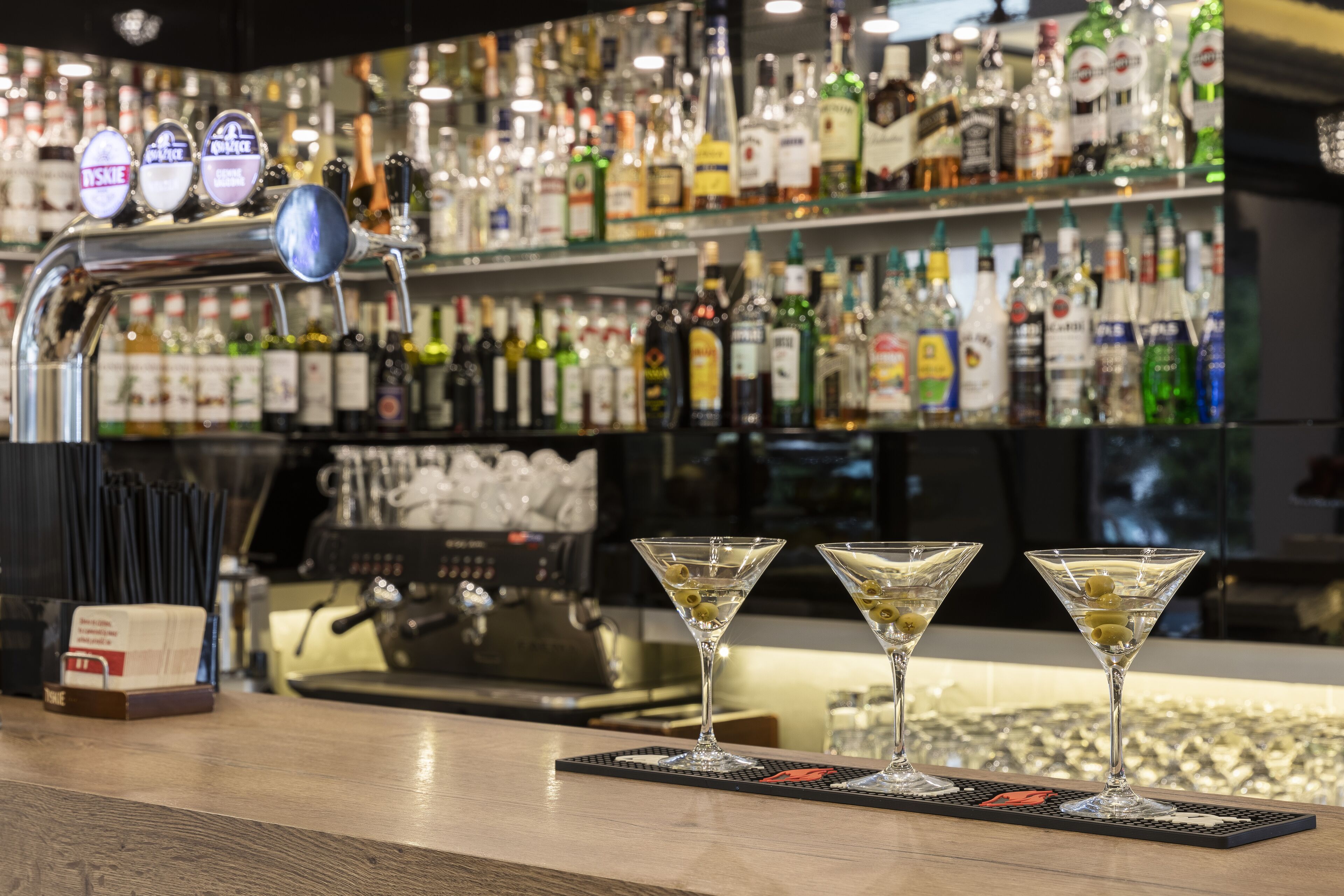 A bar area with a beer tap, two martini glasses, and a variety of liquor bottles in the background.