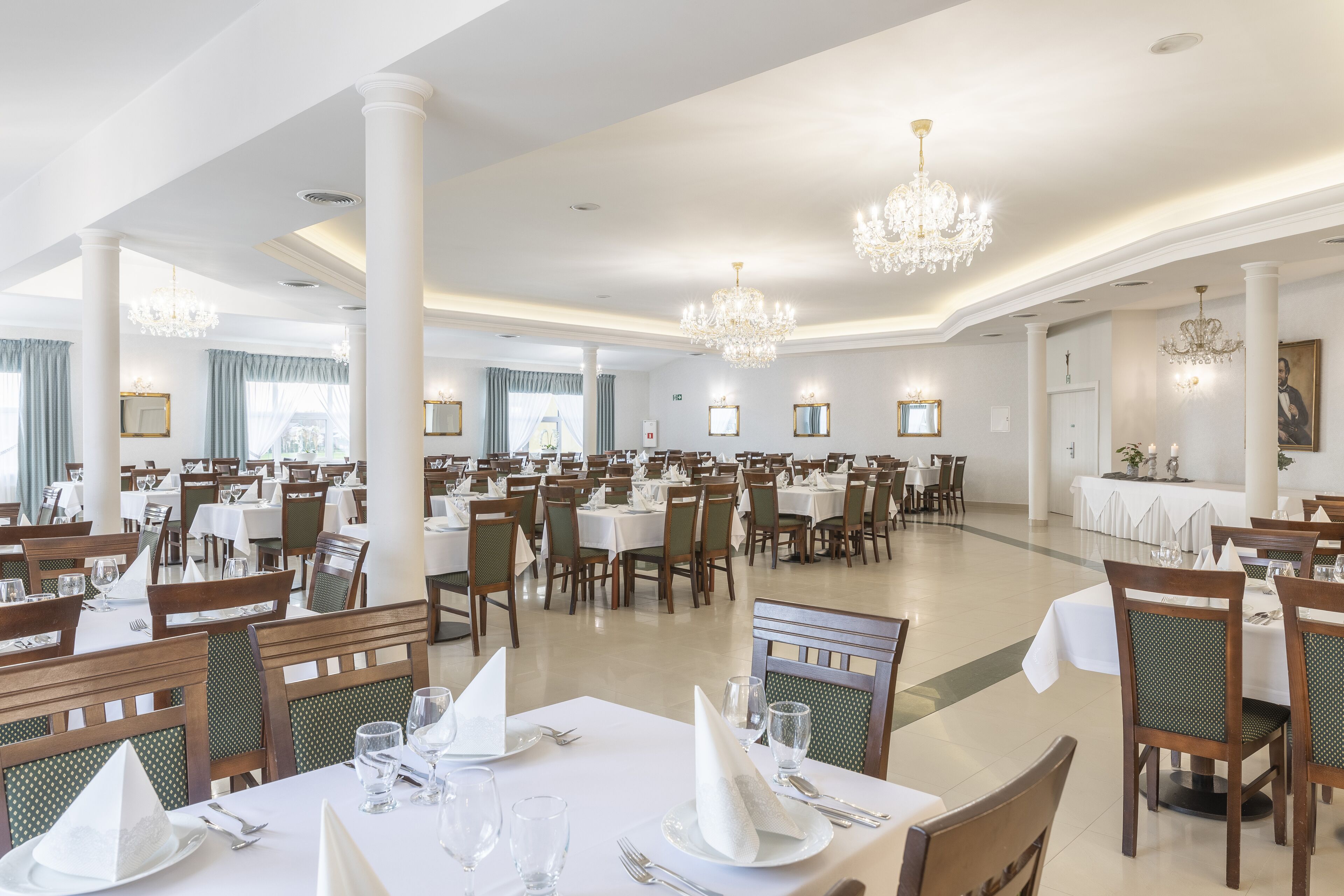 Une grande salle à manger avec de nombreuses tables et chaises, des lustres et des œuvres d’art encadrées accrochées aux murs.