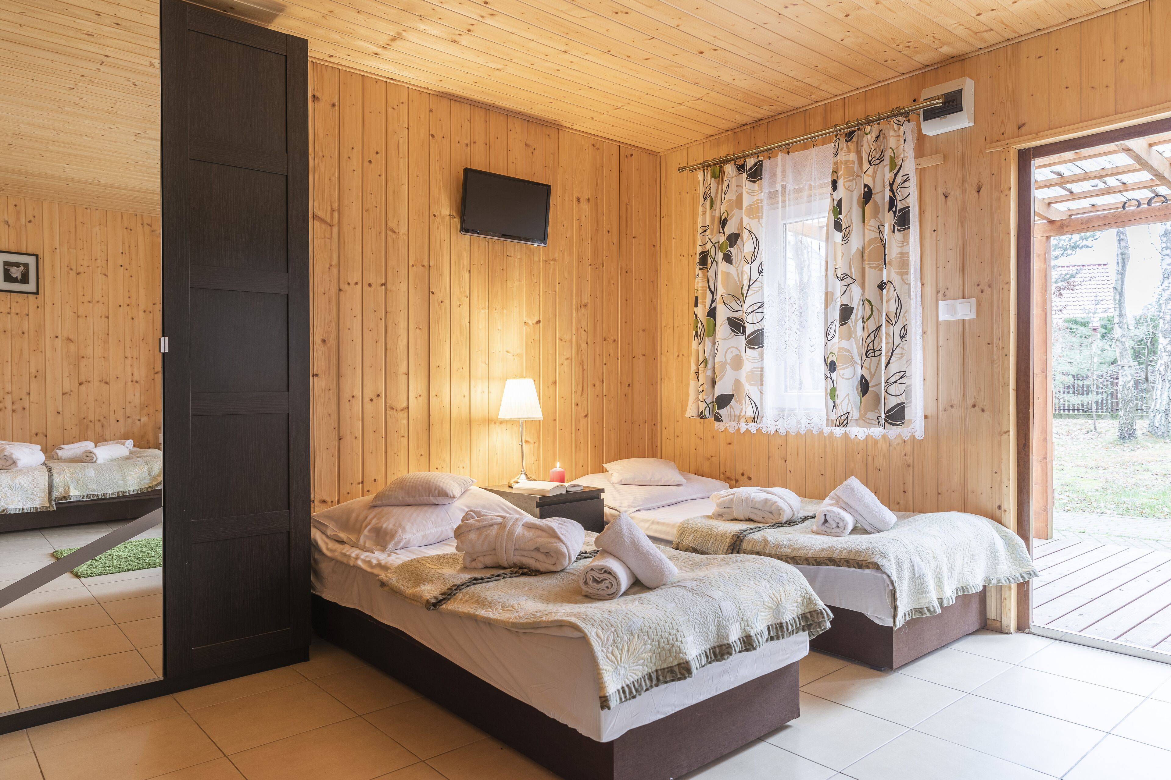 A wooden room with two beds, a TV, a window with a curtain, and a door.