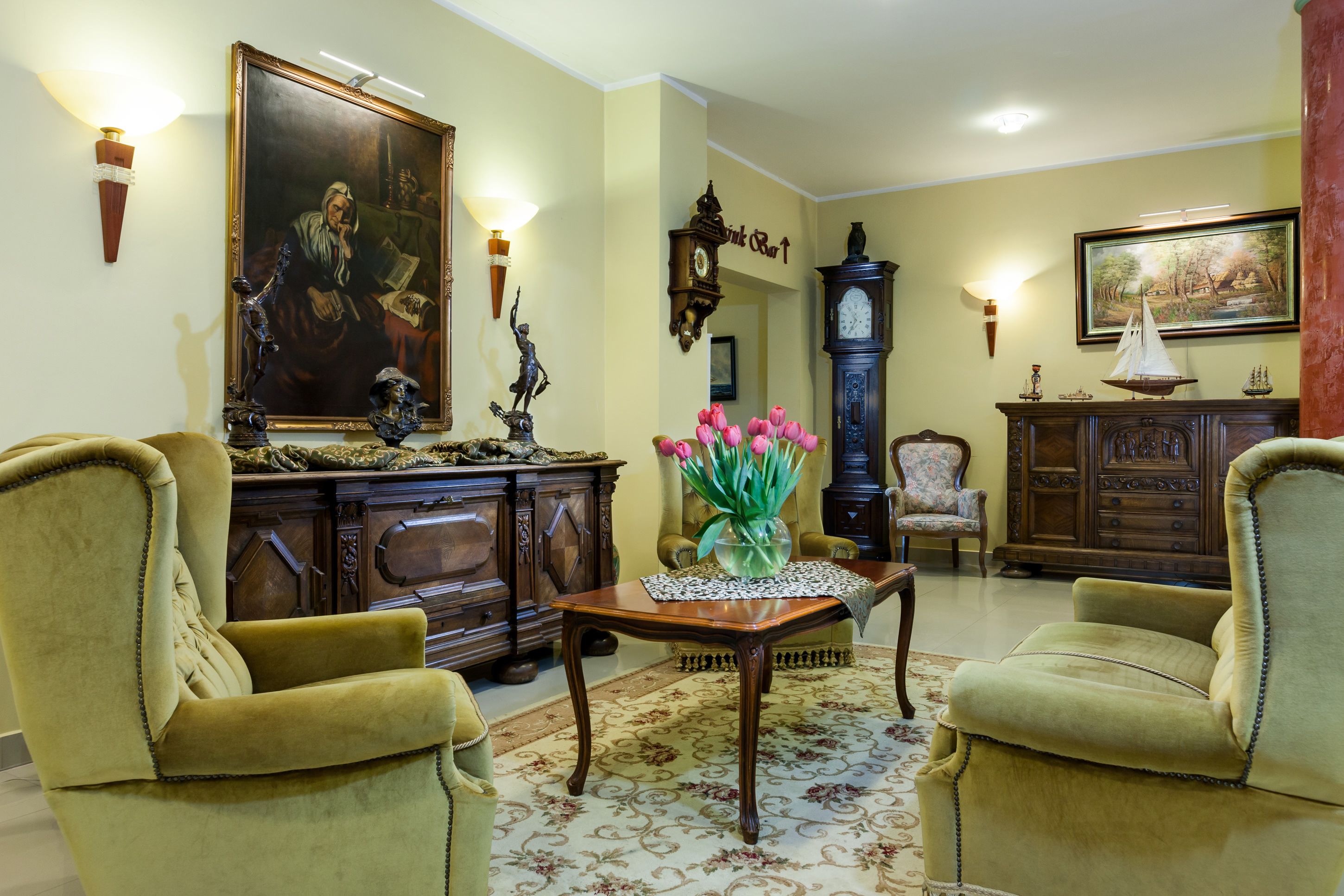 Ein traditionelles Wohnzimmer mit zwei Sesseln, einem Holztisch mit Blumenvase, einem großen Gemälde, einer Standuhr und einem Schrank mit Dekorationen.