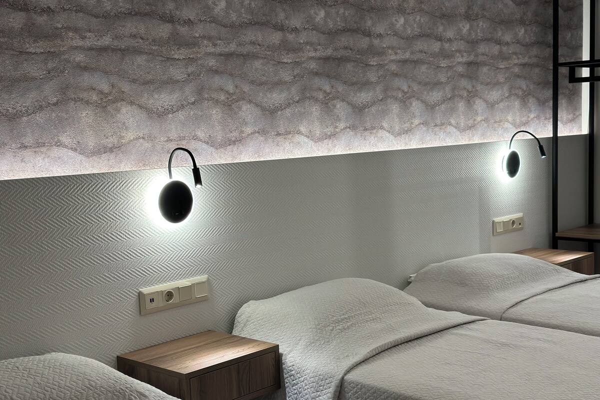 Un dormitorio moderno con dos camas, un revestimiento de pared texturizado y lámparas de lectura fijadas a la pared.