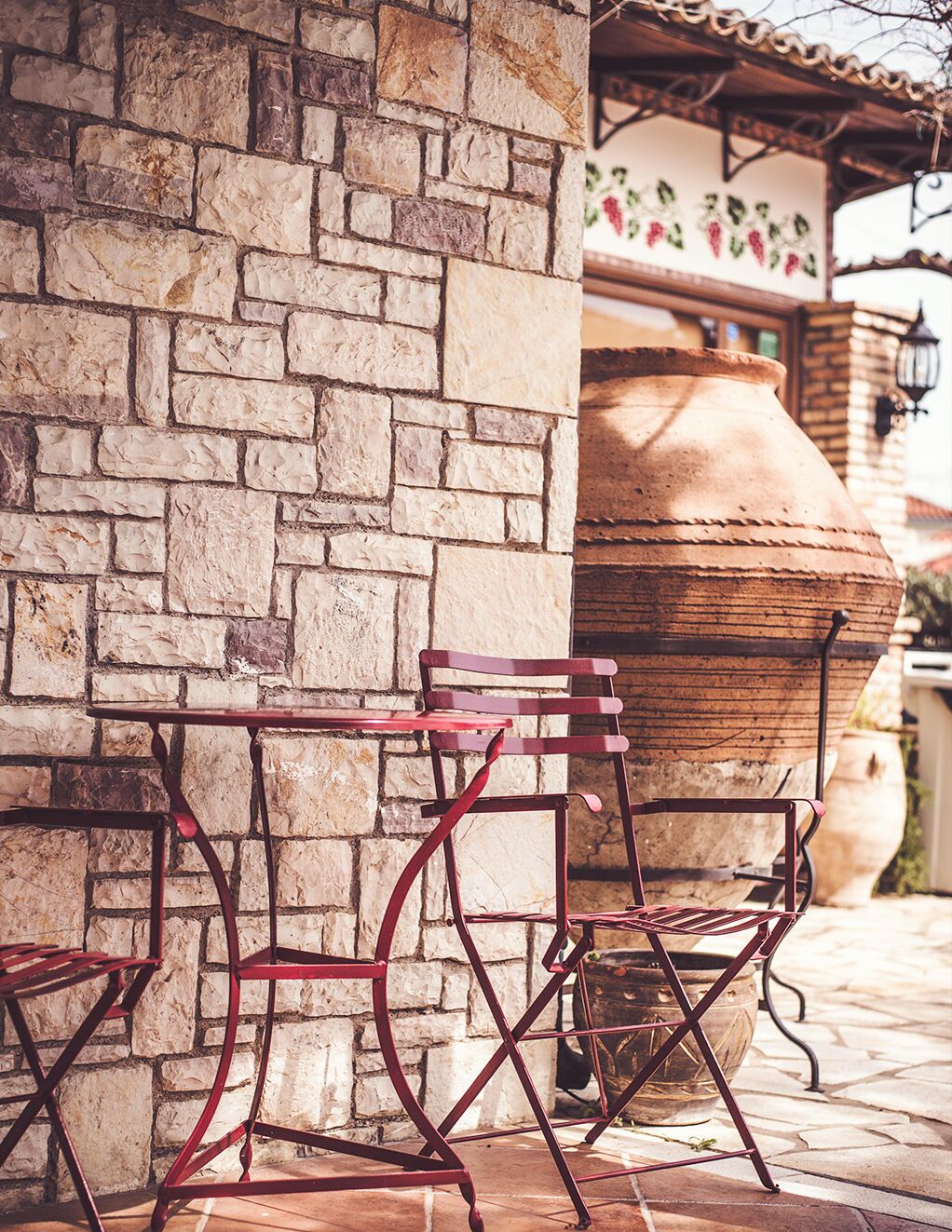 Un mur de pierre, une table et une chaise en métal, et un grand pot en argile.