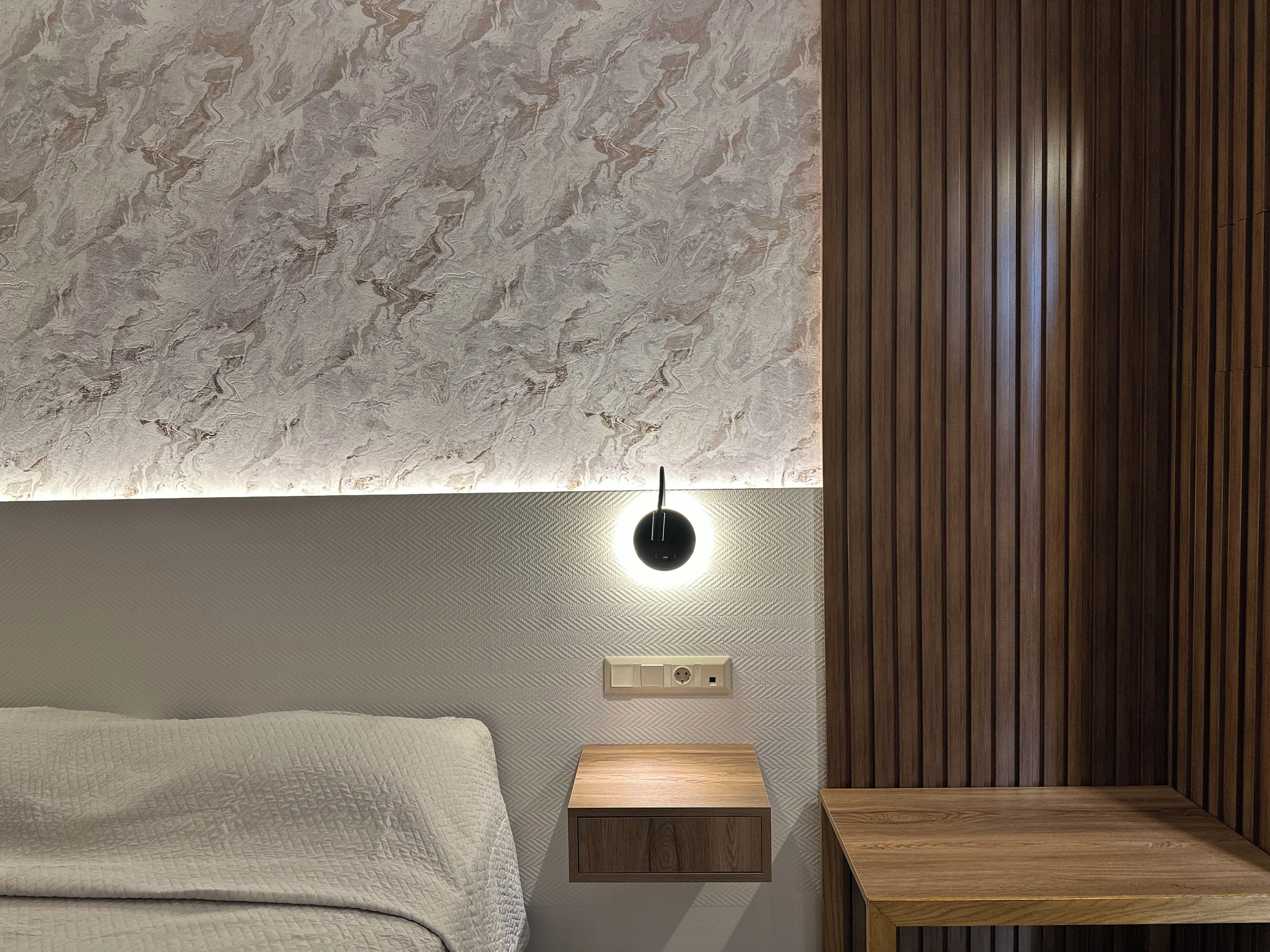 A modern bedroom with a textured wall, a bedside table, and a wooden panel wall.